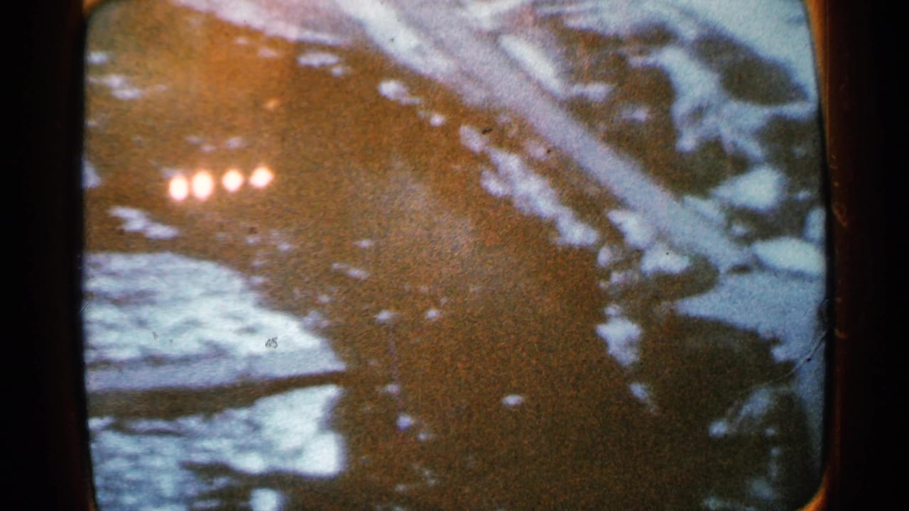 Dark icy river bordered by snow, with small bright headlights near the upper left.