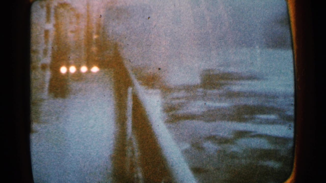 Television screen with a snowy roadway, a dark vehicle, and several bright reflected lights.