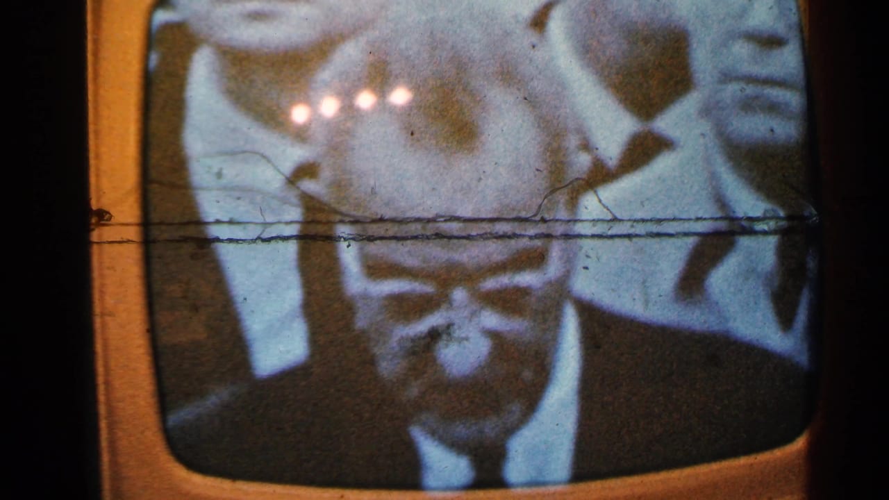 Vintage television screen showing a monochrome news broadcast with suited men and glare.