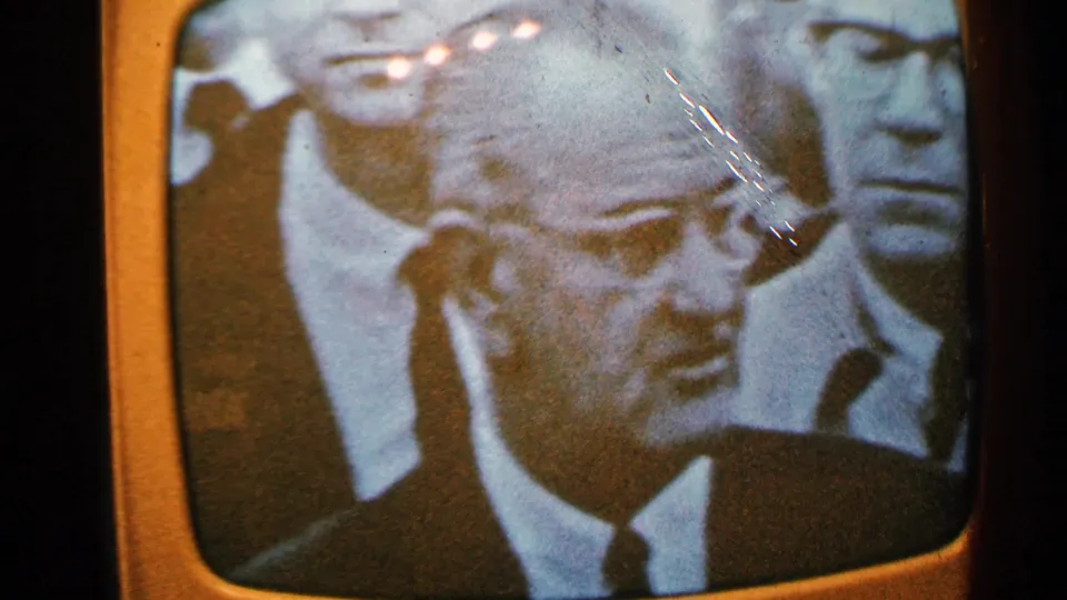 Minnesota 1965 8mm still of a vintage TV showing a black-and-white news close-up of a man in glasses, with glare and film scratches.