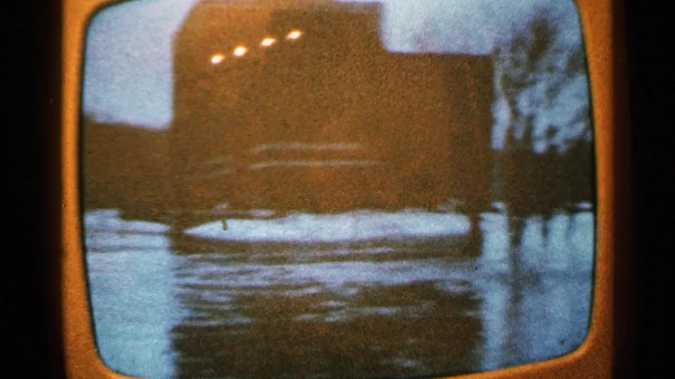 The final frame shows filmed television footage of floodwater beside a dark building-like form, with grain and color shift.