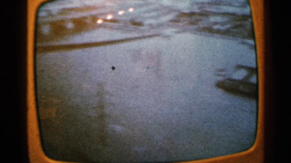 Minnesota 1965 home-movie frame showing water and possible bridge or roadway edge, softened by motion blur and projected-film texture.