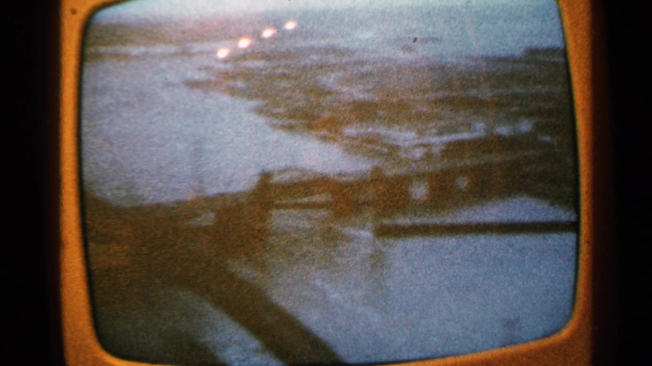 1965 Minnesota 8mm frame showing a soft aerial view of a wide river, banks, and built shoreline seen on a television screen.