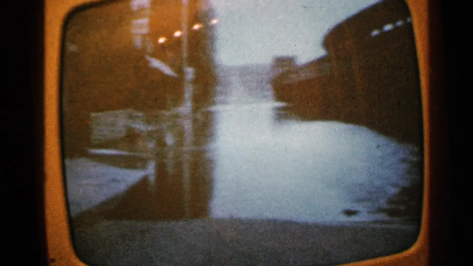 1965 Minnesota 8mm frame showing an aerial view along a river channel with dark banks and riverside structures in soft focus.