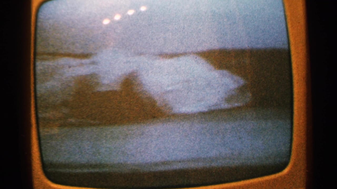 1965 Minnesota home-movie frame of a rounded TV screen displaying a soft, blue dusk shoreline or cityscape scene.