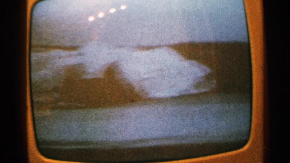 1965 Minnesota home-movie frame of a rounded TV screen displaying a soft, blue dusk shoreline or cityscape scene.