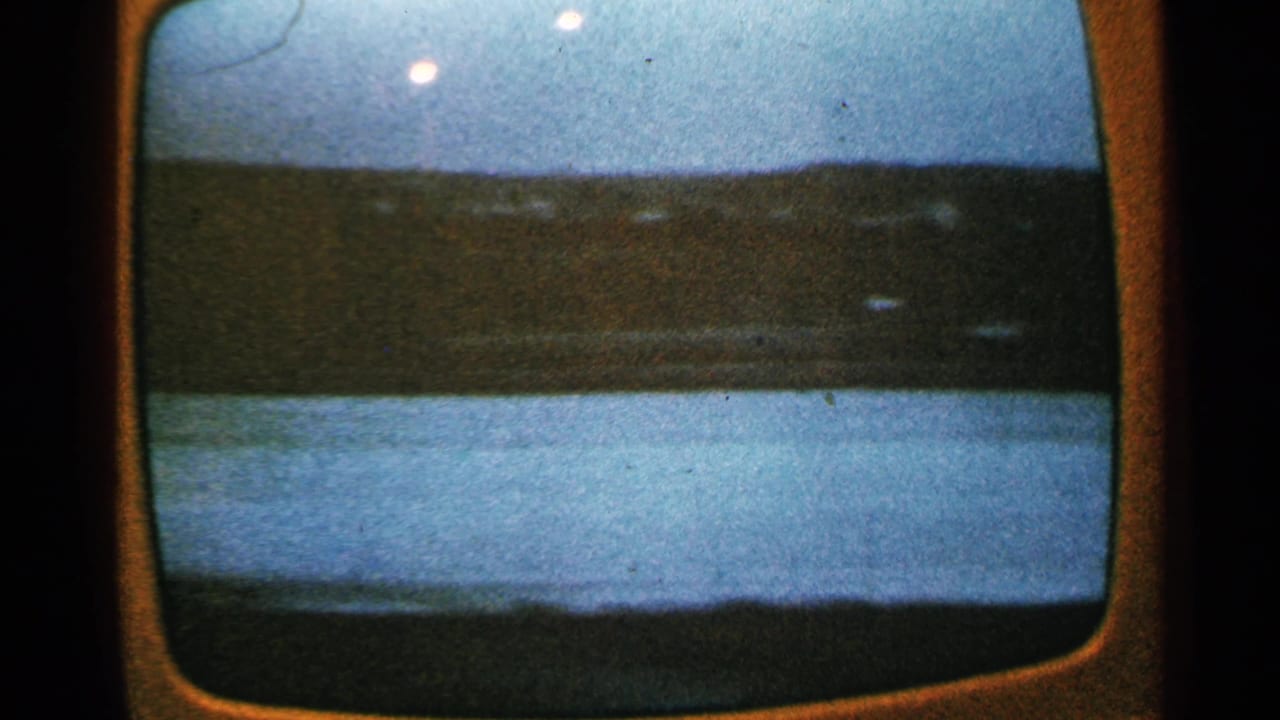 A filmed television display shows a distant dark shoreline or cityscape against a blue dusk sky in Minnesota, 1965.