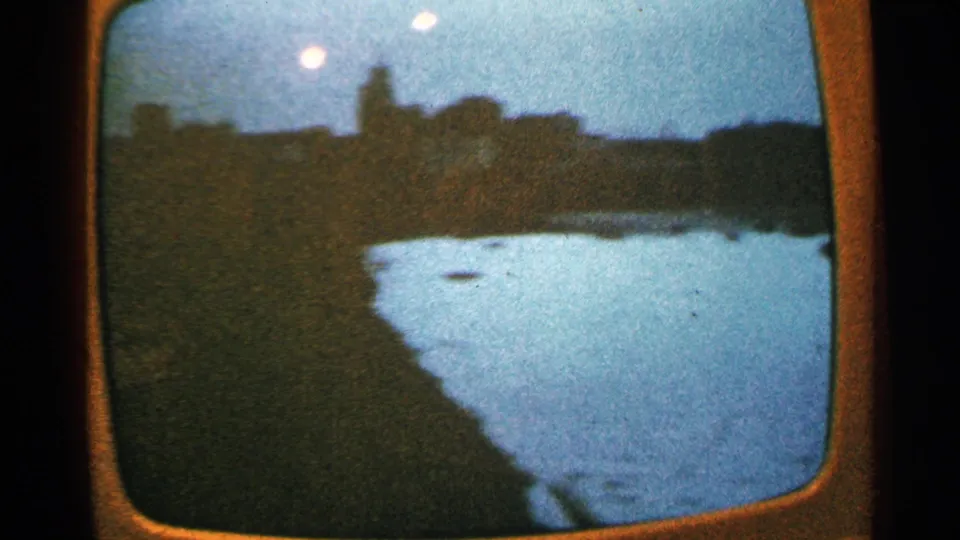 Rounded TV screen in a 1965 Minnesota home movie, showing a dark shoreline and bright curved water or ice area at dusk.