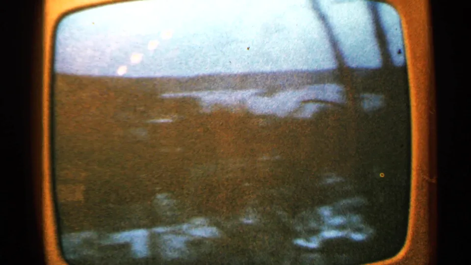 1965 Minnesota 8mm frame of a dim television landscape with low horizon, screen glare, and faint reflected shapes near the bottom.