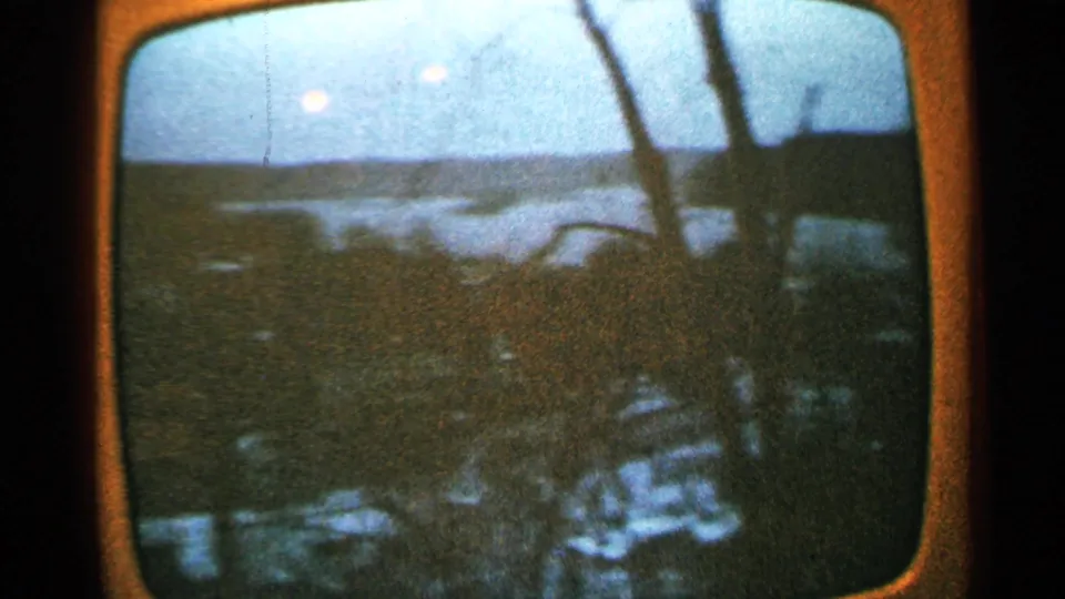 1965 Minnesota 8mm frame of a television landscape with faint human silhouettes reflected against the glowing screen.