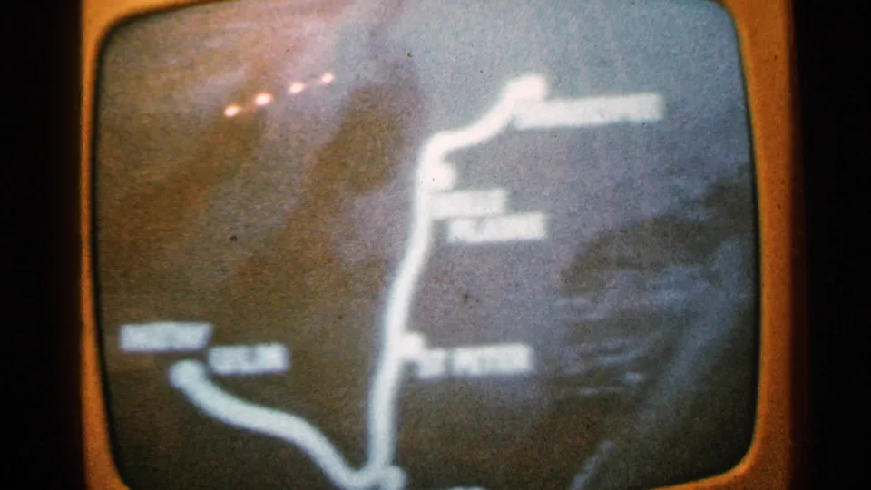 A grainy 8mm frame shows the route map closer, with a vertical white path, branching line, and labels too soft to identify securely.