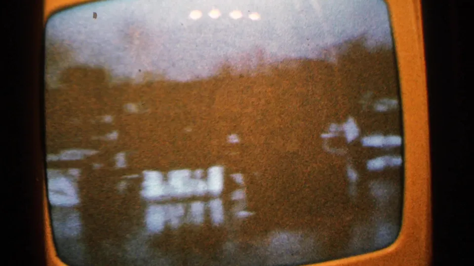 1965 Minnesota home-movie frame of a rounded TV screen showing a hazy lakeside view with trees, water, and small buildings.