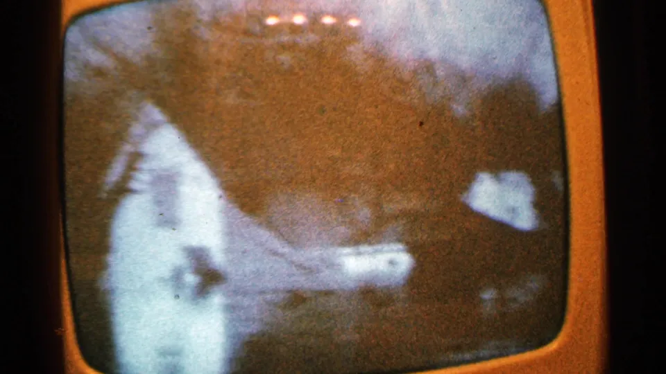 1965 Minnesota frame showing a soft, grainy TV view of a pale structure near water with dark trees behind it.