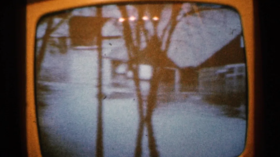 1965 Minnesota home-movie frame showing floodwater across a residential street, with bare trees and houses in soft focus.