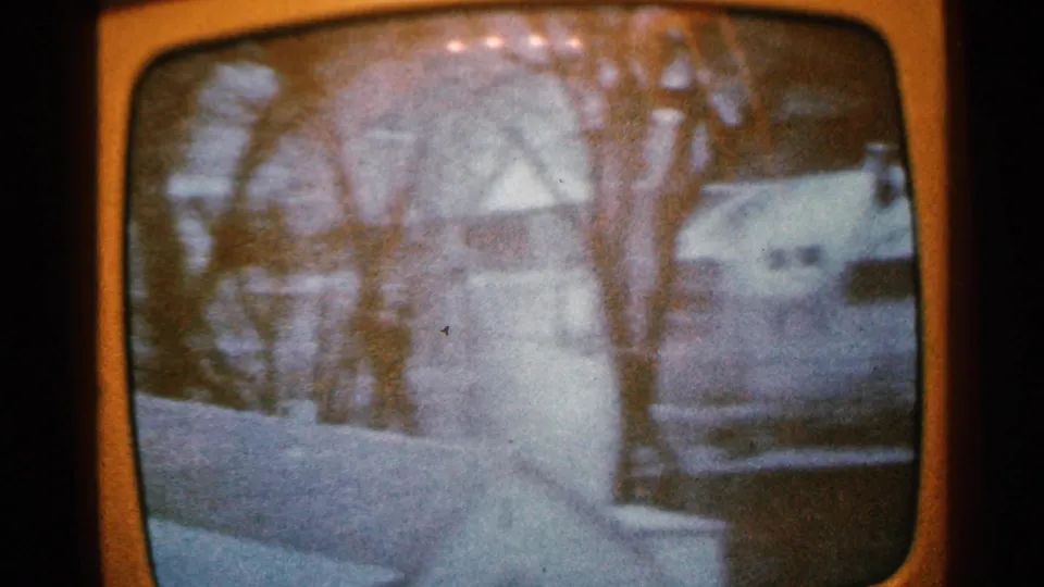 1965 Minnesota 8mm frame of a flooded residential area with bare trees, houses, and a parked car near high water.