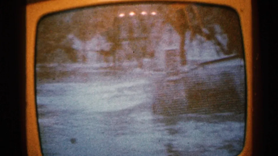 1965 Minnesota home-movie view of floodwater spread across a neighborhood street, with trees and houses visible beyond.