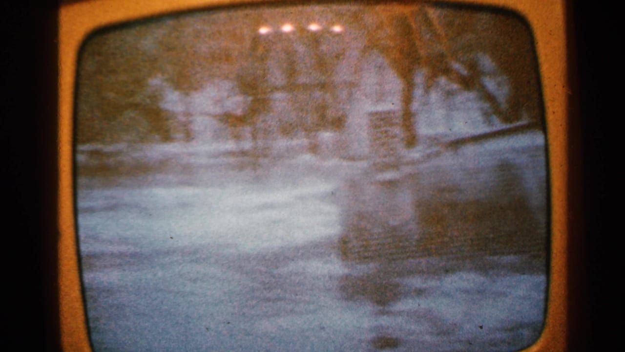 Orange television screen showing a blurry flooded scene with trees and a faint figure-like form.