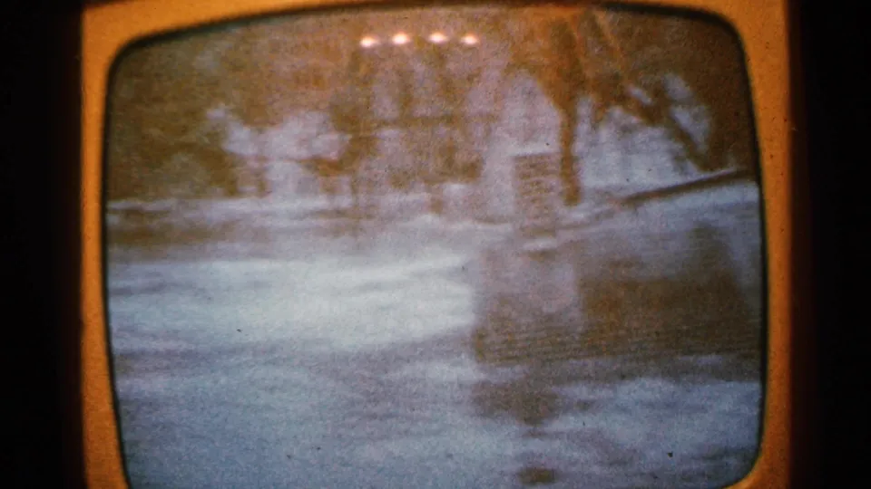 1965 Minnesota 8mm frame of an orange television set showing a grainy flooded landscape with trees and indistinct broadcast imagery.