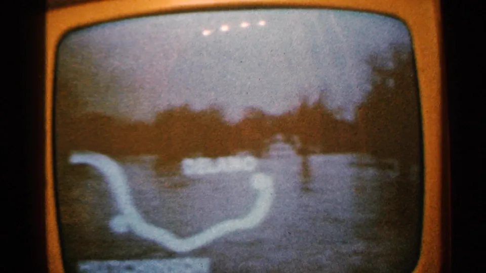 1965 Minnesota home-movie frame of an orange television showing flood imagery with a pale map-like graphic and heavy screen glare.