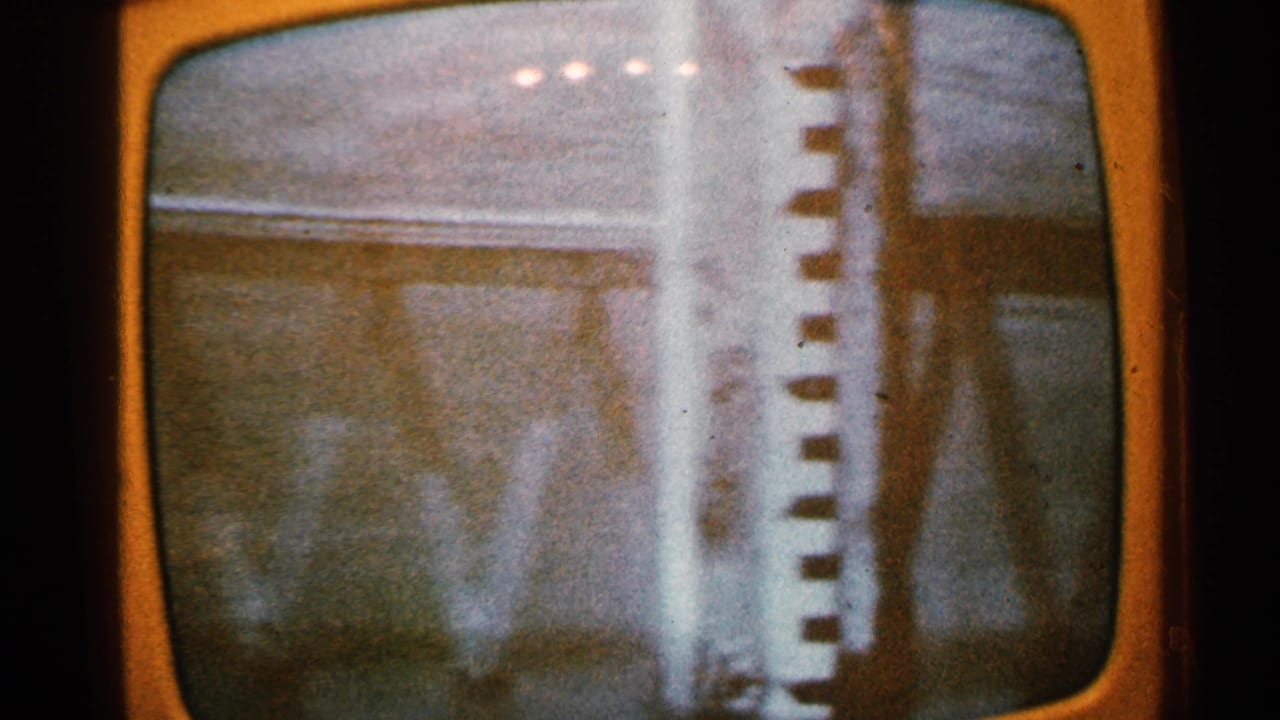 1965 Minnesota home-movie frame of a television broadcast showing floodwater near a building, with visible scan lines and screen distortion.
