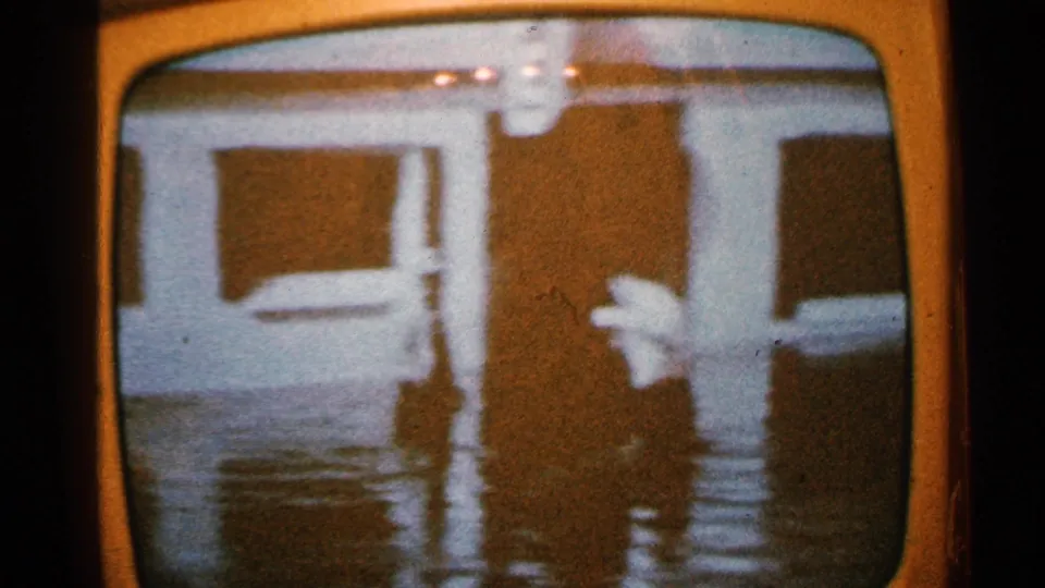 1965 Minnesota broadcast footage on a television screen shows a person wading in floodwater beside a house or low building.
