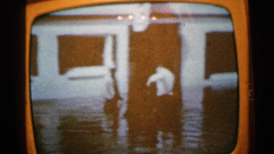 Televised 1965 Minnesota flood footage shows a person in dark clothing wading through water in front of a building.