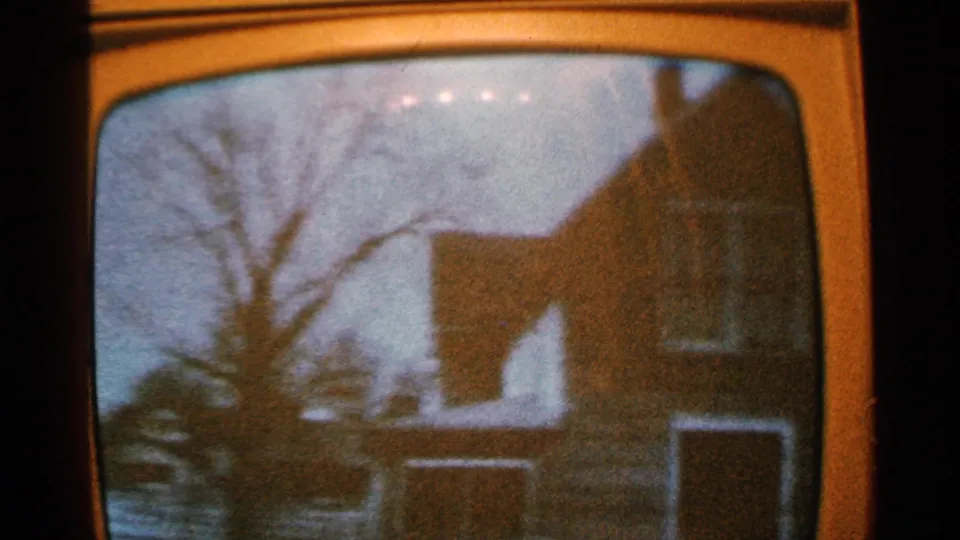 1965 Minnesota home-movie frame showing floodwater, bare trees, and residential buildings through a vintage television screen.
