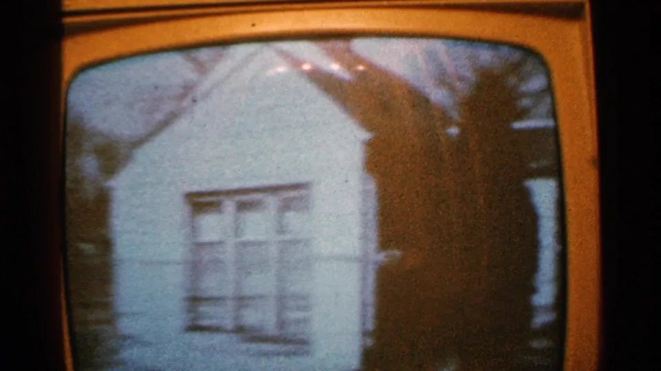 1965 Minnesota 8mm frame of a television image panning across a white house wall, a large window, and dark trees at the edge of the screen.