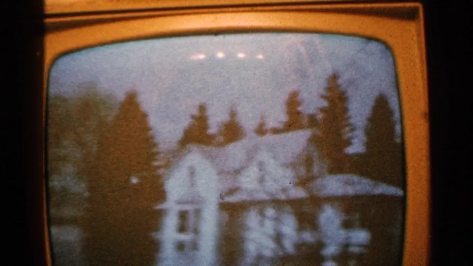 1965 Minnesota 8mm frame of a curved CRT television screen showing a snowy house with trees in soft focus.