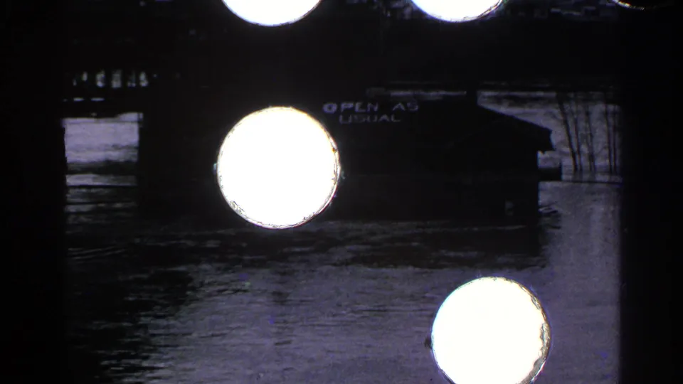 Minnesota 1965 8mm frame showing floodwater around a riverside building, partly obscured by large bright film flares.