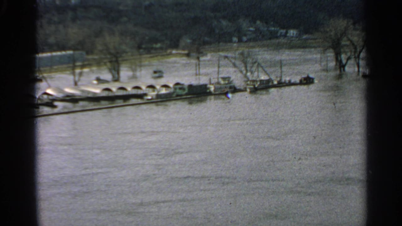 1965 Minnesota 8mm frame showing high floodwater, bare trees, and a line of boats or barges near the far bank.