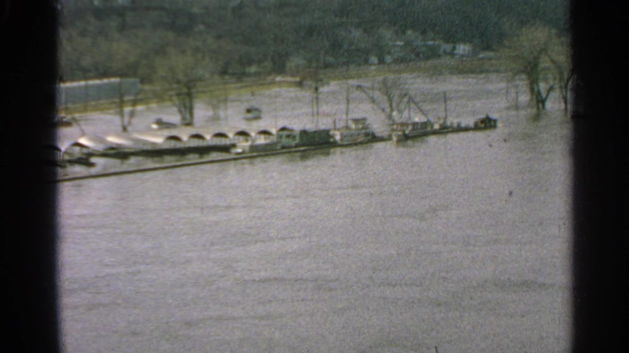 1965 Minnesota flood view with boats or barges, a crane structure, and trees standing in high water.
