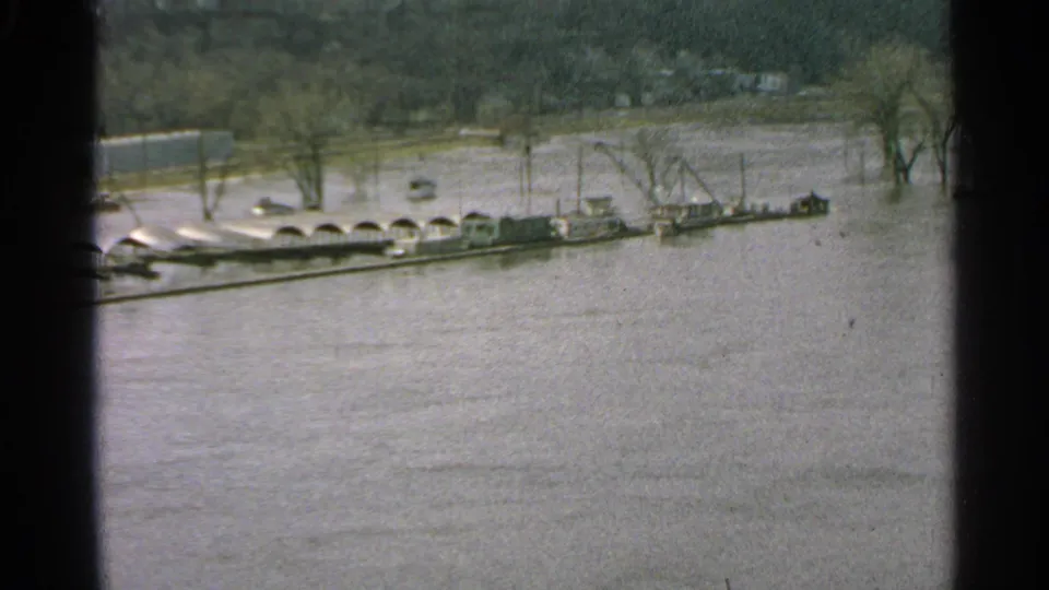 1965 Minnesota flood view with boats or barges, a crane structure, and trees standing in high water.