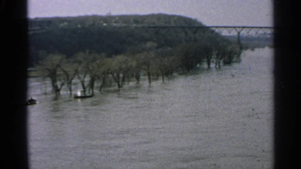 1965 Minnesota 8mm frame of trees partly underwater, broad floodwater, wooded hills, and a distant bridge.