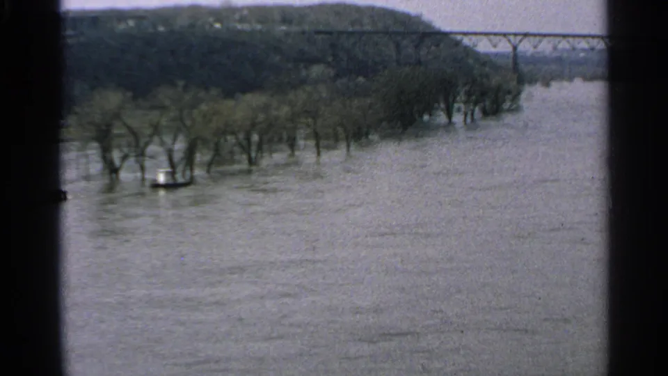 1965 Minnesota 8mm view of high river water, flooded trees along the bank, and a steel truss bridge in the distance.