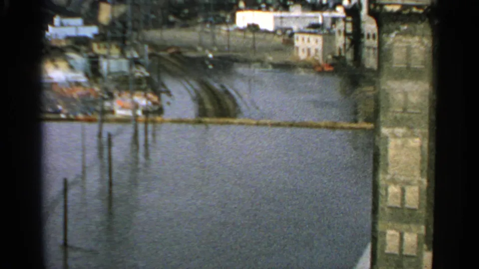 1965 Minnesota 8mm view of a flooded street or rail corridor with water around buildings and utility poles in a residential or industrial area.