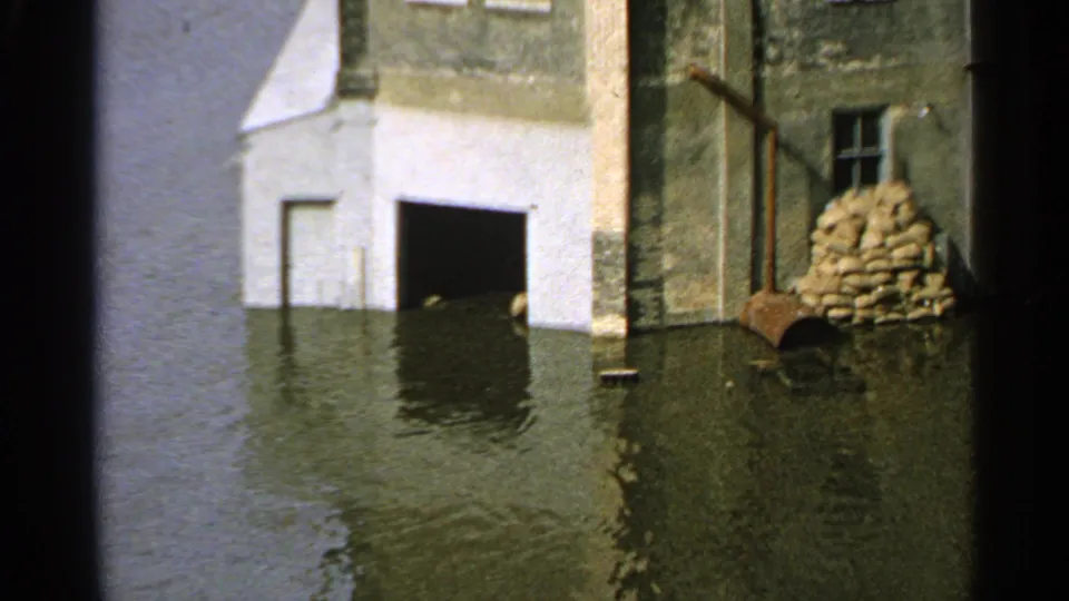 1965 Minnesota flood close view of a building partly surrounded by water, with sandbags stacked beside the wall and a dark doorway at water level.