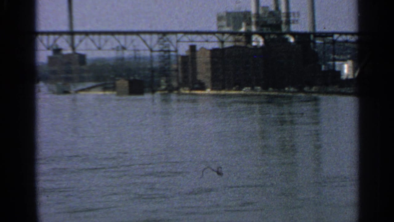 Factory buildings and a bridge across calm river water.