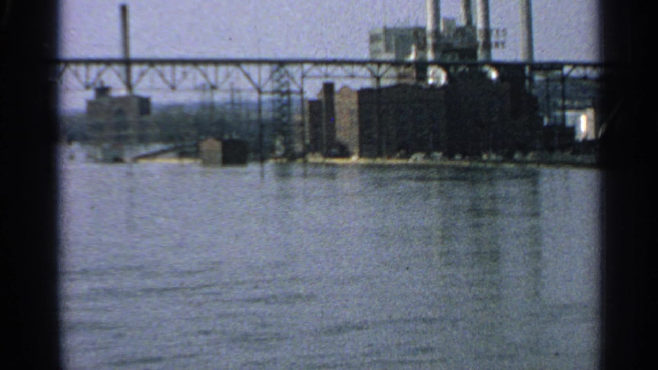 Bridge span and factory complex seen across the water.