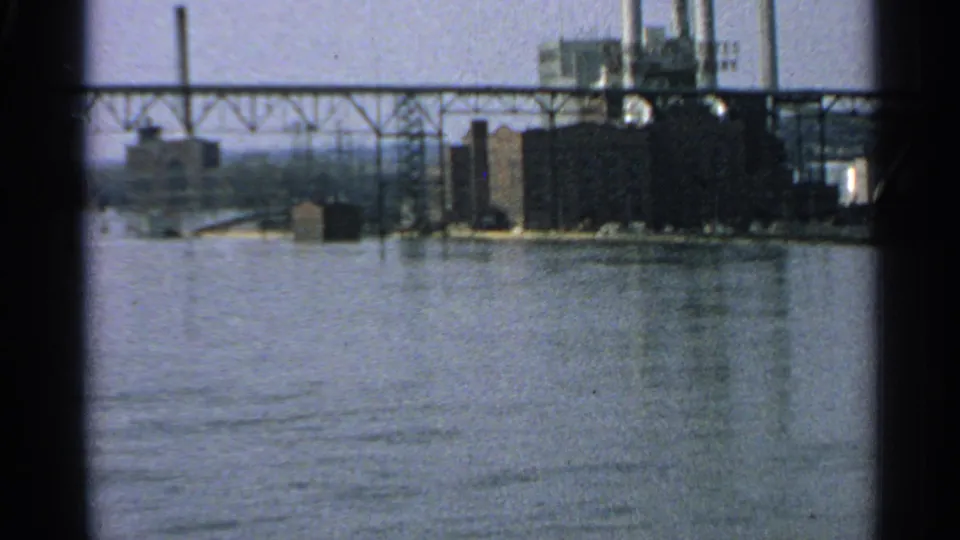 Industrial riverfront in Minnesota, with a bridge crossing the frame and factory buildings beyond the water.