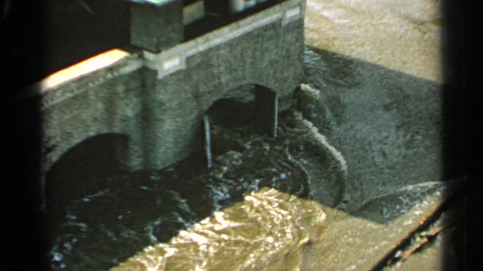 1965 Minnesota 8mm frame showing turbulent floodwater pushing through arched bridge openings from an elevated viewpoint.