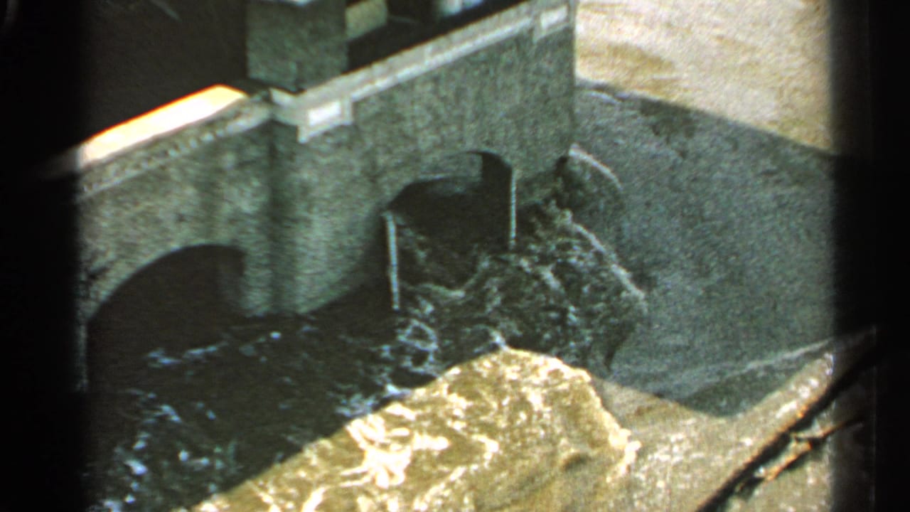 Fast water churns below a masonry bridge with arched openings.