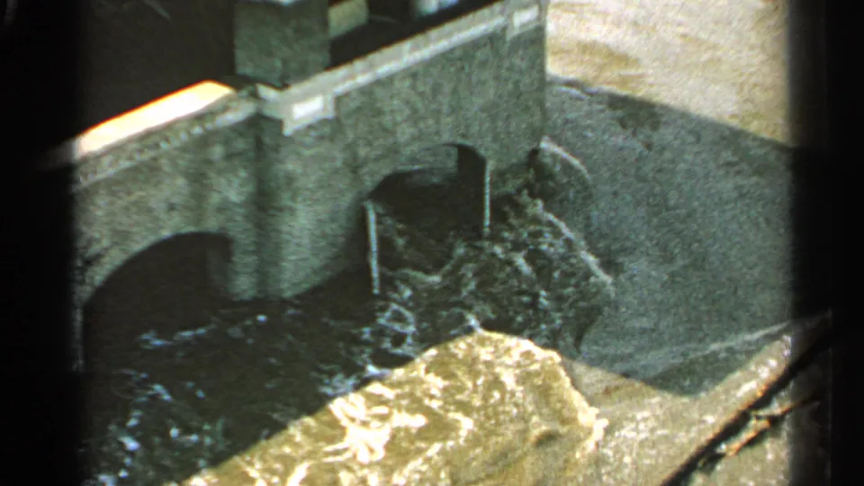 Elevated 1965 Minnesota view of muddy floodwater foaming beneath a stone or concrete arched structure.