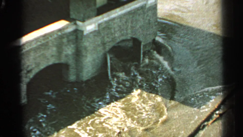 1965 Minnesota home-movie frame of floodwater frothing near the base of an arched bridge or culvert structure.