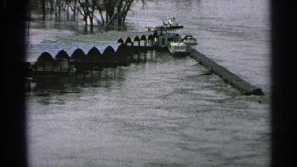 1965 Minnesota frame showing high water around a long pier, small boats, and shoreline structures.