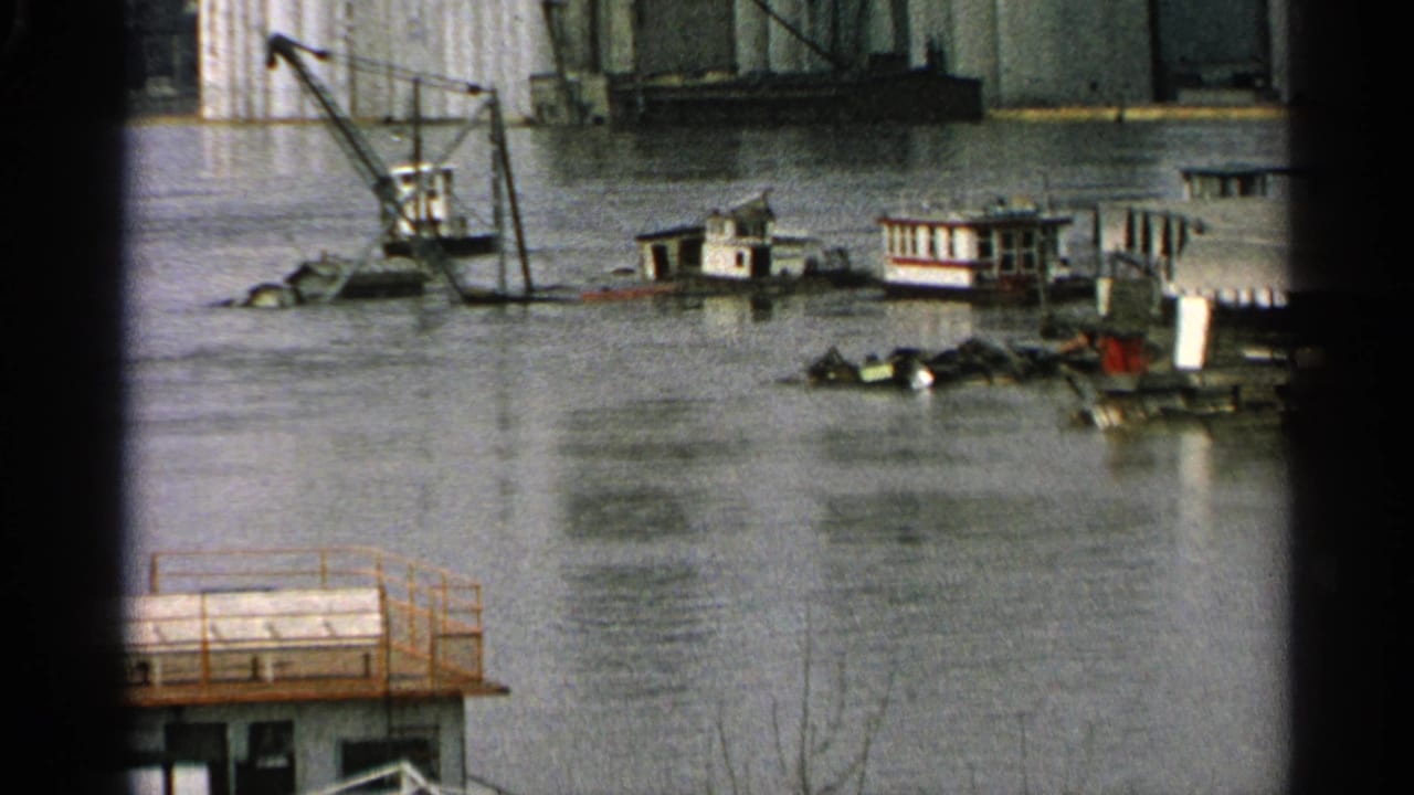Minnesota 1965 8mm view of a flooded industrial or construction area with barges, crane equipment, and debris in murky water.