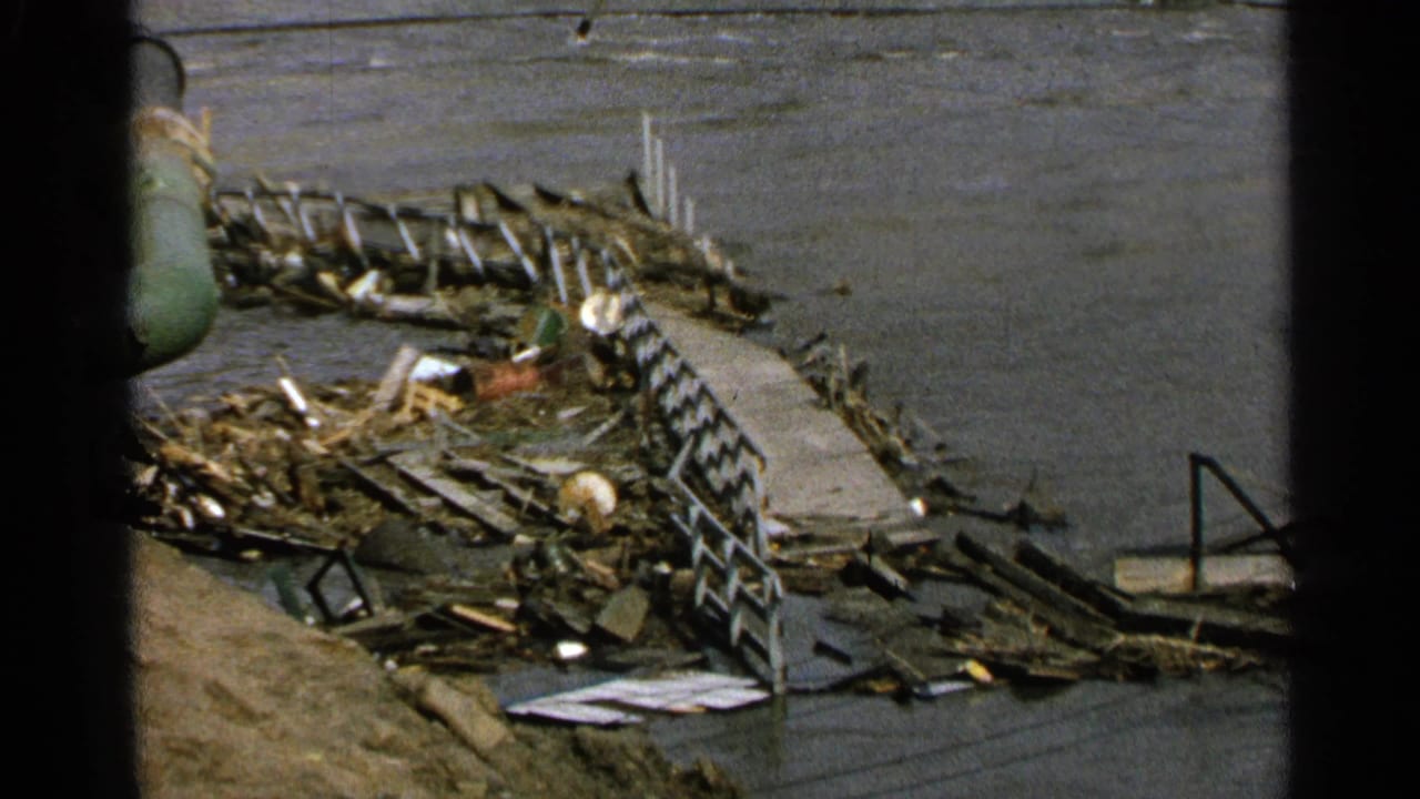 Damaged dock area with debris piled along the water and a green pipe at the left edge.
