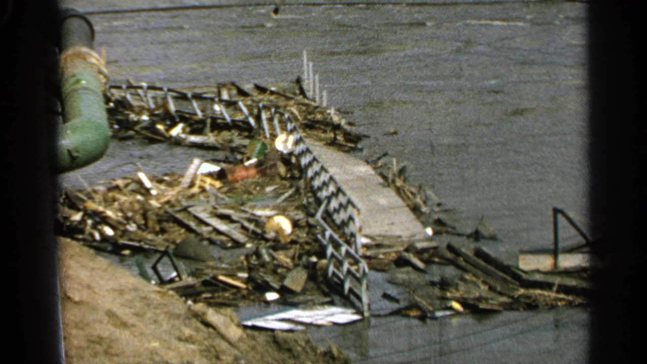 Waterfront debris surrounds a broken dock with railings and a green pipe near the left side.