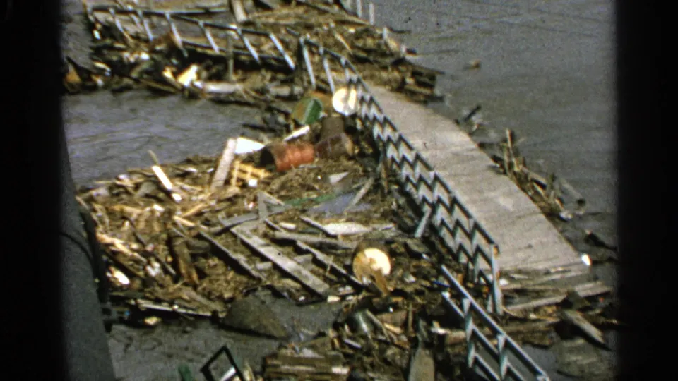 Minnesota 1965 8mm frame with a closer view of a damaged dock edge, railings, piled debris, and water behind the wreckage.