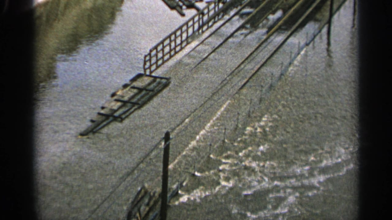 1965 Minnesota flood scene with moving water, metal railings, and industrial structures partly surrounded by high water.